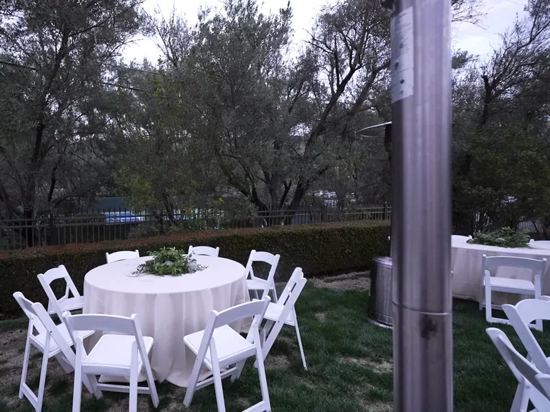 White linen round tables and folding chairs set on a lawn shaded by oaks near Livermore