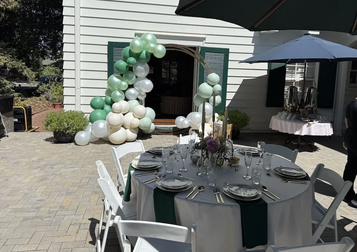 Sage and ivory balloon garland over a doorway paired with a bloom-accented tablescape — balloon and floral styling for Danville catering celebrations