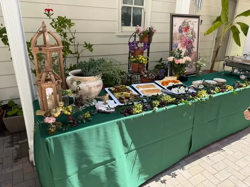 Pleasanton private-party buffet featuring a green tablescape, charcuterie selections, floral accents, lanterns, and seasonal fruit.